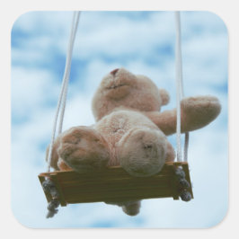 Beertje op schommel met bewolkte blauwe lucht. quadratischer aufkleber