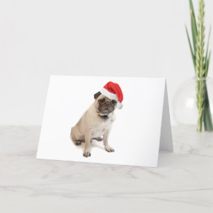 Beige Mops mit roter Weihnachtsmannmütze auf Feiertagskarte