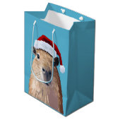 Capybara feierlich in Weihnachtsmannmütze Mittlere Geschenktüte (Vorderseite Schrägansicht)