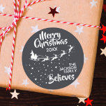 Christmas Santa’s sleigh reindeers holiday Runder Aufkleber<br><div class="desc">Zeigen Sie, wie sehr Sie an den Zauber von Weihnachten und Weihnachtsmann glauben, mit diesem Weihnachtsfamilienrundaufkleber, der die Silhouette des Schlittens des Weihnachtsmanns in Weiß mit seinen Rentieren zeigt und auf Sternenwegen fliegt. Die Titelschrift auf oben liest Frohe Weihnachten in weißer handgeschriebener Schrift. Der Text ist leicht an Ihre Wünsche,...</div>