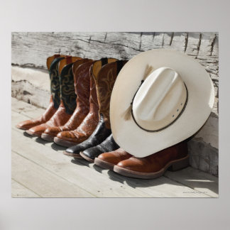 Cowboy-Hut in Reihe von Cowboy-Stiefeln außerhalb  Poster