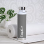 Dark Gray Personalisiert Wedding Bridesmaid Trinkflasche<br><div class="desc">Gönnen Sie Ihrer Hochzeitsjury oder Ihrer Trauzeugin diese trendige, vakuumisolierte Wasserflasche, die ihren Namen in weißem, stylisiertem Schrift auf einem dunkelgrauen Hintergrund hat, der zu Ihrem Hochzeitsfarbenschema passt. Stellen Sie die Flasche nach Belieben durch Bearbeiten und Ersetzen des Namens durch Ihren eigenen Namen ein. Wählen Sie Ihre Wasserflasche. Erhältlich in...</div>