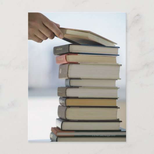 Die Hand des Mannes, die ein Buch von einem Stapel Postkarte (Vorderseite)