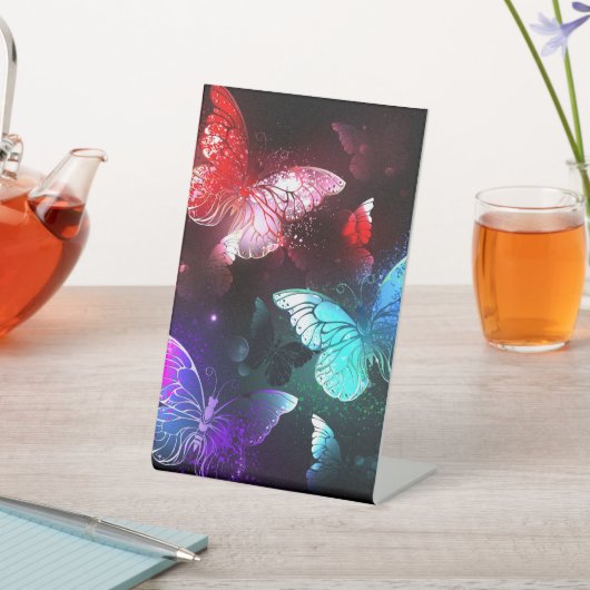 Drei glühende Schmetterlinge im Hintergrund Sockelschild (In SItu)