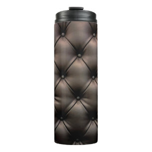 Ein dunkles Lederkissen als Hintergrund, von einem Thermosbecher