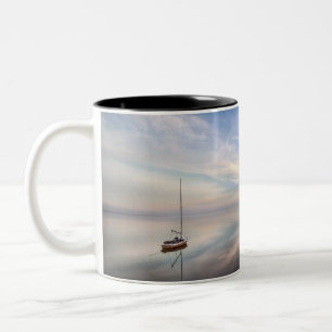 Ein einziges Segelboot auf dem ruhigen Wasser von Zweifarbige Tasse