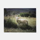 ein kleines weißes Lamm hinter einem Zaun auf eine Fußmatte (Vorderseite)