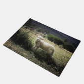 ein kleines weißes Lamm hinter einem Zaun auf eine Fußmatte (Schrägansicht)