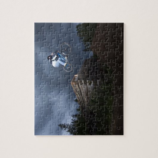 Ein Mountainbiker springt von einer Blockhütte in Puzzle (Vertikal)