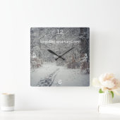 Ein schneebedeckter Weg durch einen Winterwald Quadratische Wanduhr (Zuhause)
