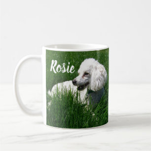Ein weißes Poodle, das sich in üppig grünem Gras r Kaffeetasse