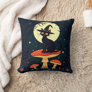 Eine kleine schwarze Hexenkatze sitzt auf einem Fl Kissen