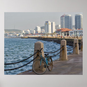 Fahrrad am Wasser mit der Skyline der Stadt Yantai Poster