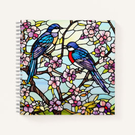 Farbenfrohe, festgeklemmte Glasvögel auf blühenden Notizblock
