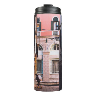 FRAU IN WEISSEN SHIRT- UND SCHWARZPANTEN, DIE AUF  THERMOSBECHER