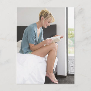 Frau liest ein Buch auf dem Bett Postkarte