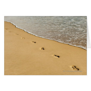 Fußdrucke im Sand mit Welle
