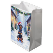 German Pinscher Snowy Courtyard Santa Hat Mittlere Geschenktüte (Rückseite Schrägansicht)