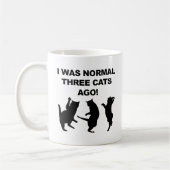 Gewöhnliche drei Katzen sind vor lustiger Umarmung Kaffeetasse (Links)