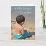 Grandson Birthday, Junge am Strand Karte<br><div class="desc">Eine Geburtstagskarte für einen Großsohn mit einem Foto eines dunkelhaarigen Jungen mit hellblauen Hosen,  der im Sand am Strand mit etwas weiter entferntem Wasser sitzt.</div>