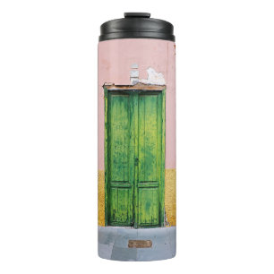 GRÜNE HOLZTÜR AN DER WEISSEN KONKRETEN WAND THERMOSBECHER