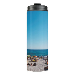 GRUPPE VON MENSCHEN, DIE DEN GRAUEN SANDSTRAND GEN THERMOSBECHER