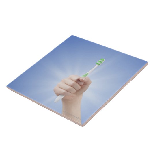 Hand, die Zahnbürste hält Fliese (Seite)