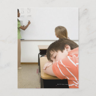 Junge, die auf einem Schreibtisch im Klassenzimmer Postkarte