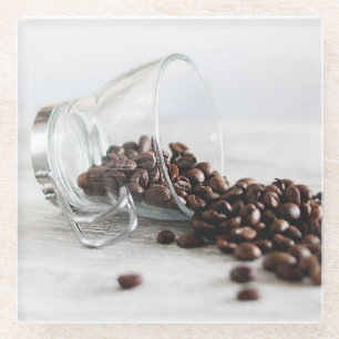 Kaffeebohnen, die sich aus einem klaren Kaffeecup Glasuntersetzer