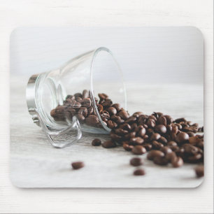 Kaffeebohnen, die sich aus einem klaren Kaffeecup Mousepad
