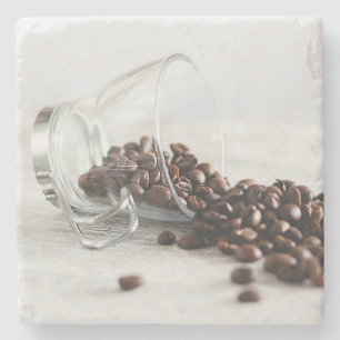 Kaffeebohnen, die sich aus einem klaren Kaffeecup Steinuntersetzer