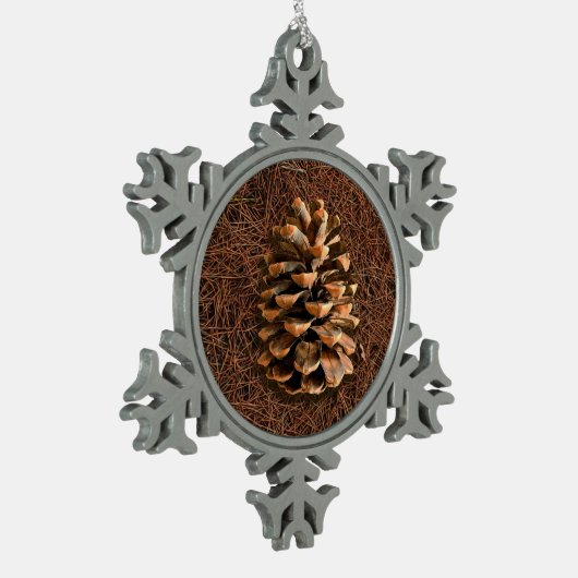 Kiefernkone auf gefallenen Nadeln Schneeflocken Zinn-Ornament (Links)