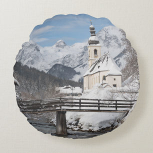 Kirche im Schnee mit den Alpen im Winter Rundes Kissen