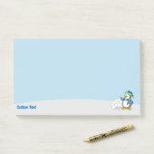 Kleiner Pinguin mit Schneeballschuhen, der nach de Post-it Klebezettel (Auf Schreibtisch)