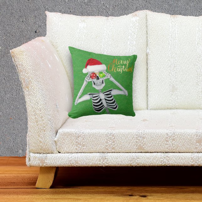 Lächeln Skeleton Holding Ornamente an Augen Grün Kissen (Happy Merry Christmas Skeleton in Santa hat with ornaments on green throw pillow.)