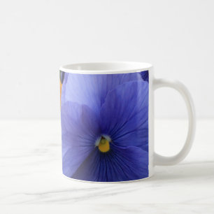 Lila und orangefarbene Stiefmütterchen mit grünem Kaffeetasse