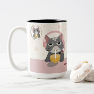 Lustige müde Katze mit Kopfhörern trinkt Orangensa Zweifarbige Tasse