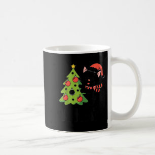 Lustige schwarze Katze schiebt Weihnachtsbaum über Kaffeetasse