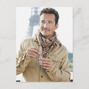 Mann mit einem Einwegbecher mit Eiffel Postkarte