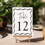 Moderne Creme- und Black Wavy-Rahmen-Hochzeit Tischnummer<br><div class="desc">Fügen Sie Ihrer Hochzeitsfeier eine stilvolle Touch mit den Hochzeitskarten Modern Wavy Frame hinzu! Das Retro-Design zeigt "Table" in einem handgeschriebenen schwarzen Skript mit der unten abgebildeten Tischnummer an. Die Tischnummer ist von einem schwarzen, welligen Rand umgeben, der mit einem hellen cremefarbenen Hintergrund kontrastiert. Das Design wiederholt sich auf der...</div>