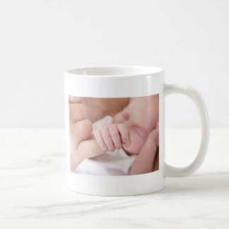 neugeborenes Baby, das Vaterfinger hält Kaffeetasse