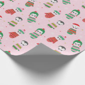 Niedliche Weihnachtspinguine in Fingern in hellros Geschenkpapier (Ecke)