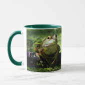 Niedlicher grüner Frosch schlägt eine Pose auf dem Tasse (Links)