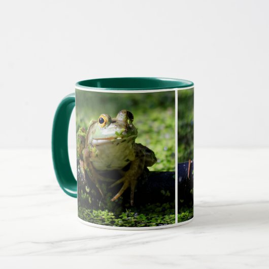 Niedlicher grüner Frosch schlägt eine Pose auf dem Tasse (Vorderseite Links)