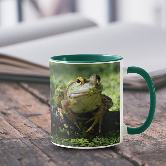 Niedlicher grüner Frosch schlägt eine Pose auf dem Tasse