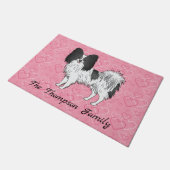 Niedlicher Hund aus schwarz-weißem Papillon auf ro Fußmatte (Schrägansicht)