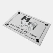 Niedlicher Hund aus schwarz-weißem Papillon mit be Fußmatte (Schrägansicht)