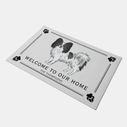 Niedlicher Hund aus schwarz-weißem Papillon mit be Fußmatte (Schrägansicht)