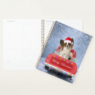 Papillon Hund im Schnee sitzen im Weihnachtswagen Planer