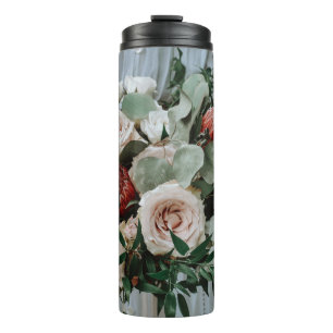 PERSON, DIE DIE ROTE BLUME UND PINKENBOUQUET BESIT THERMOSBECHER